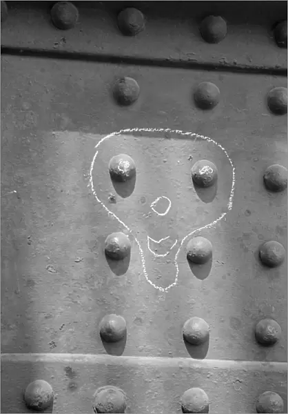 Face drawn in chalk around metal rivets, London Docks a064944