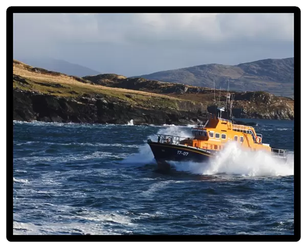 Valentia severn class lifeboat John and Margaret Doig 17-07. Lifeboat is moving from right to left in choppy seas, lots of white spray and waves breaking against cliffs in the background