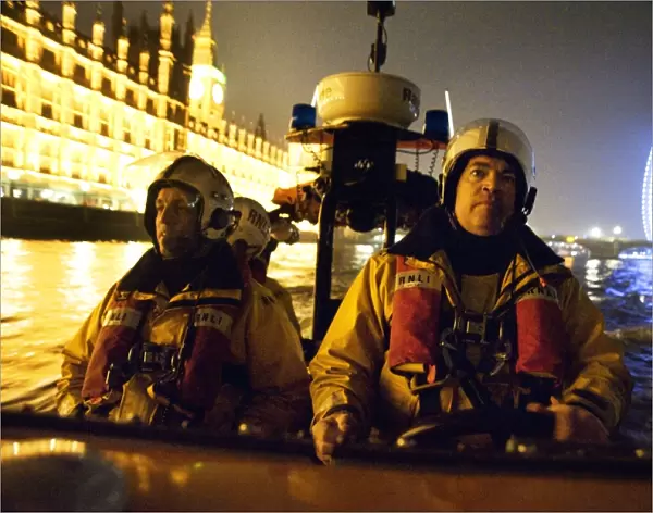 Tower lifeboat crew members on board an E-class lifeboat on the River Thames at night, Houses of Parliament and the London Eye in the background