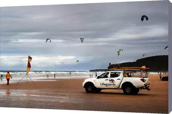Lifeguards monitoring the beach from a patrol vehicle, lots of kites in the distance