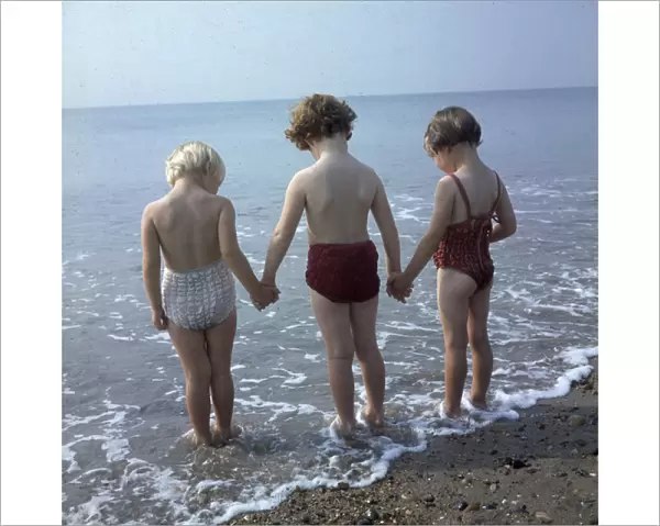 Three children holding hands, paddling in the sea
