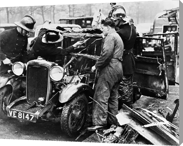 Firemen and mechanic with burnt-out car, London