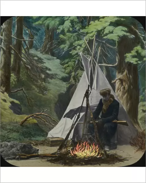 Young man sits by fire outside his teepee in the woods