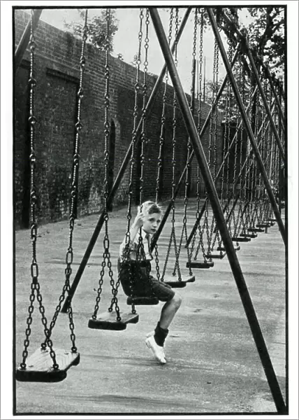Young boy alone on a playground swing 1939