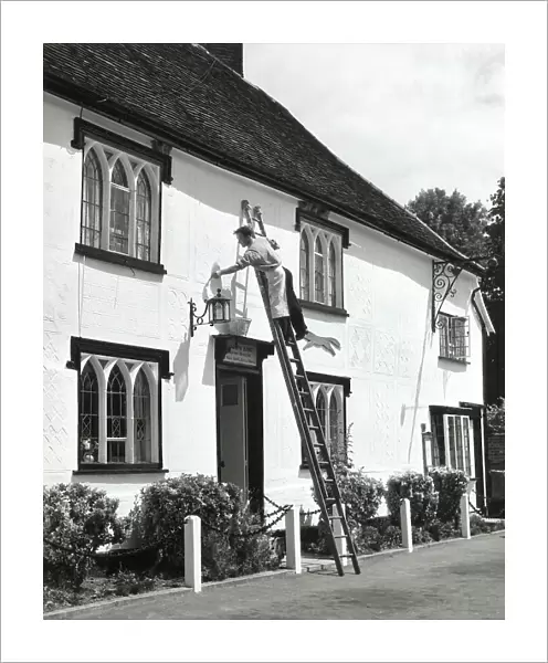 The village decorator, busy painting the front of 'The Fox' Inn, at Finchingfield, Essex, England. Date: 1960s