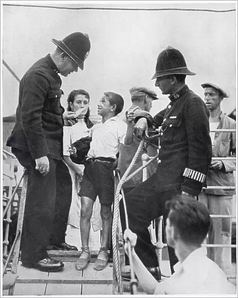 Two members of Gibraltar's police force questioning a Spanish boy on the gang-way of a refugee boat, August 1936. The Spanish Civil War, which started in the summer of 1936, meant that thousands of Spaniards became refugees