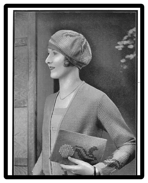 Model wearing an embroidered jacket and carrying a matching embroidered pochette, made of perforated wool net fabric. Date: 1920s
