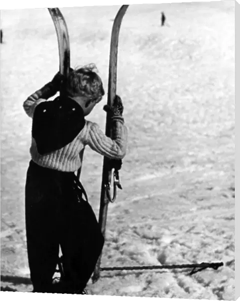 BOY SKIER. A little boy holding up a large pair of skis. Date: 1930s