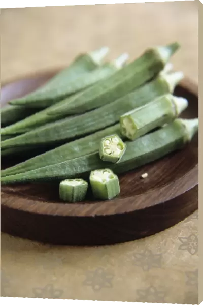 Okra pods in a bowl. One of the pods has been cut into slices to reveal