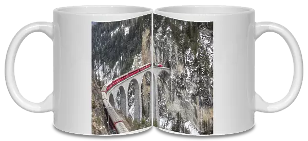 Bernina Express passes over Landwasser Viaduct, UNESCO World Heritage Site, and snowy woods