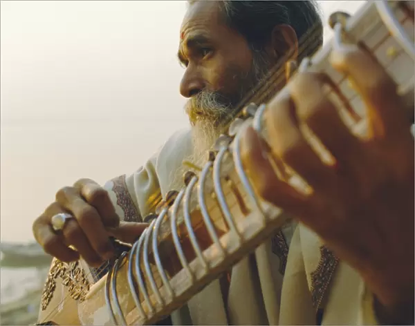 Elderly man playing the sitar beside the Ganges (Ganga) River