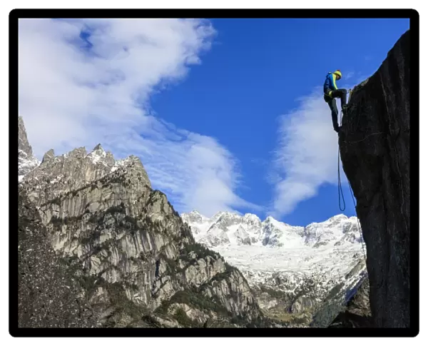 Climber on steep rock face in the background blue sky and snowy peaks of the Alps