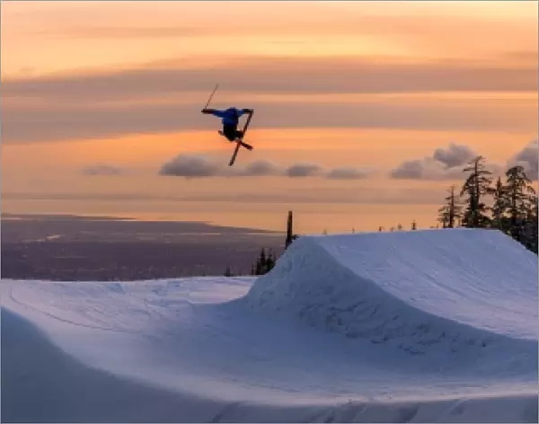 Freestyle skier doing a trick off a jump above city at sunset, Canada, North America