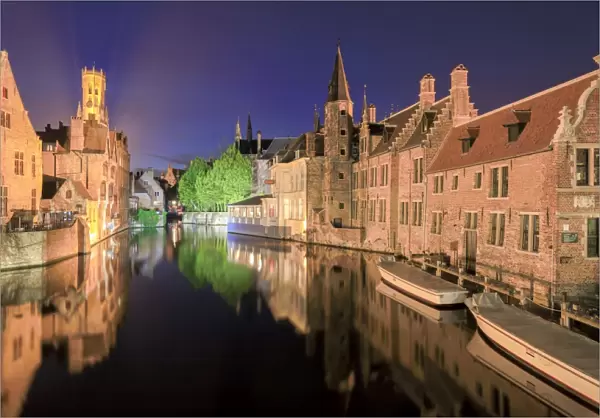 The medieval Belfry and historic buildings are reflected in Rozenhoedkaai canal at night