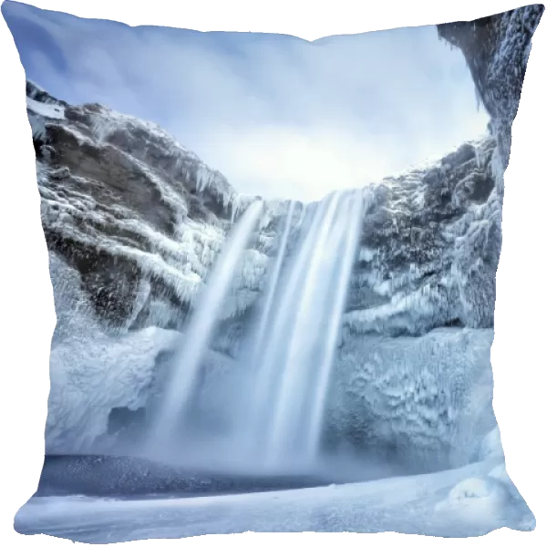 Winter view of Skogafoss waterfall, with cliffs covered in icicles and foregreound covered in snow