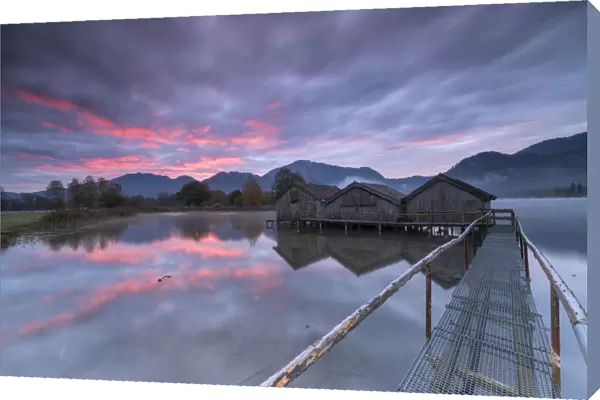 Purple sky at sunset and wooden huts are reflected in the clear water of Kochelsee