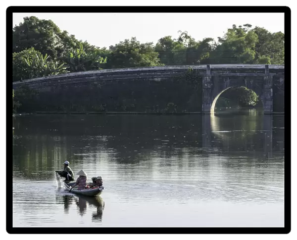 A man and woman fishing from a small boat in the moat around the Citadel in Hue, Vietnam