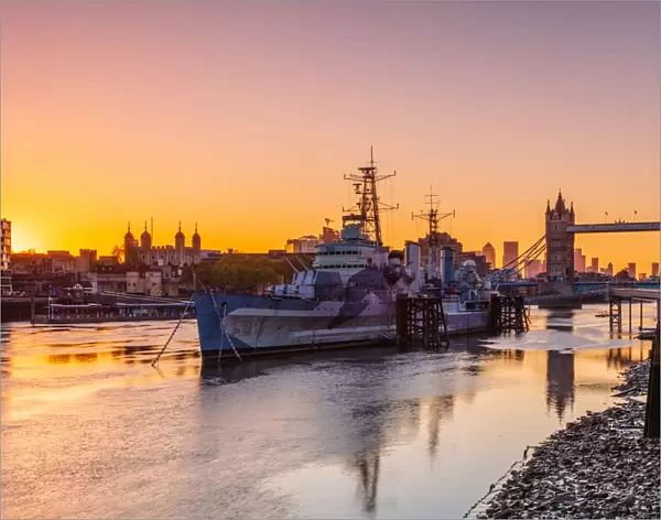 HMS Belfast and Tower Bridge at sunrise with a low tide on the River Thames, London