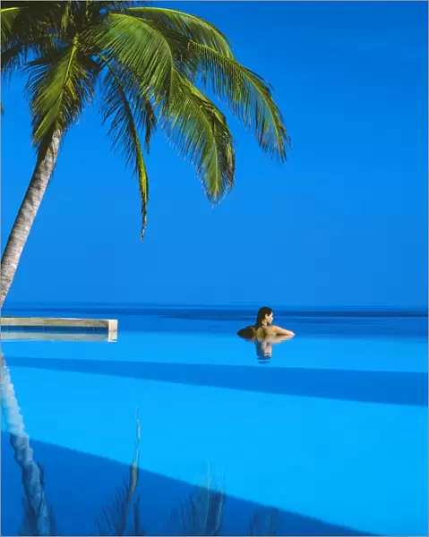 Woman in swimming pool under palm tree looking at sea, Maldives, Indian Ocean, Asia