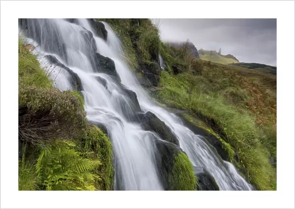 Waterfall cascading down grassy slope with Old Man of Storr in background