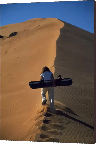 An adventurer climbs a sand dune with a sand board