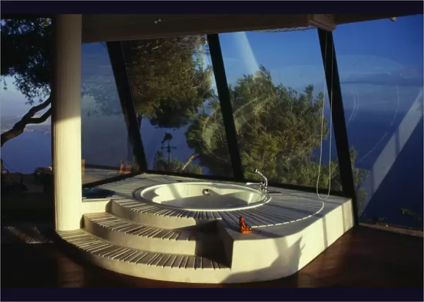 Sunken bath in sunlit room with panoramic glass windows