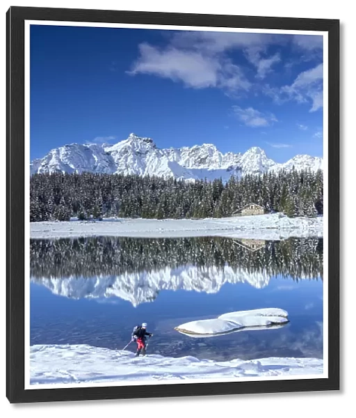 Hiker proceeds on the shore of PalA'A¹ Lake surrounded by snowy peaks and woods Malenco Valley Valtellina Lombardy Italy Europe