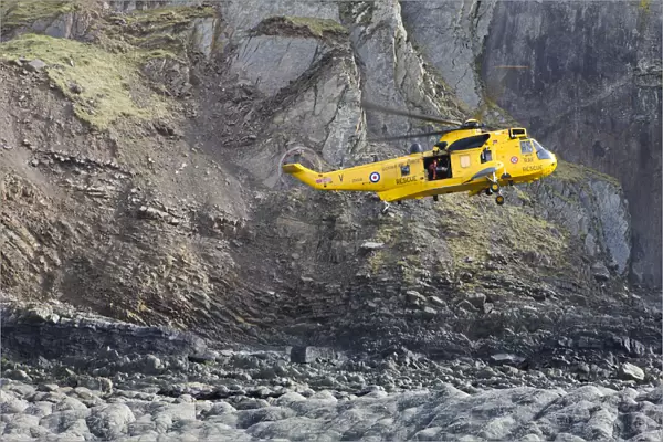 RAF helicopter performing a coastal rescue at the base of the steep cliffs of Spekes