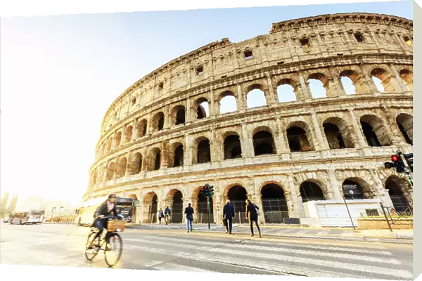 Italy, Rome, a woman riding a bike Colosseum and Roman Forum at sunrise
