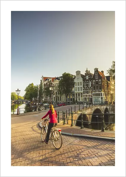 A woman riding a bike on a bridge over a canal in Amsterdam at sunset