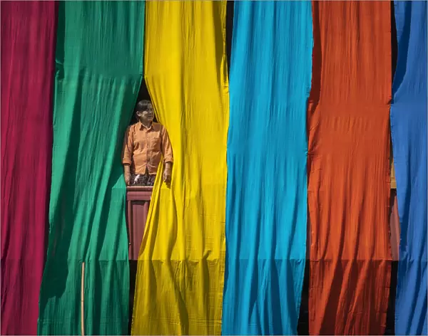 Woman in a window checking freshly dyed fabric hanging from bamboo poles to dry on a