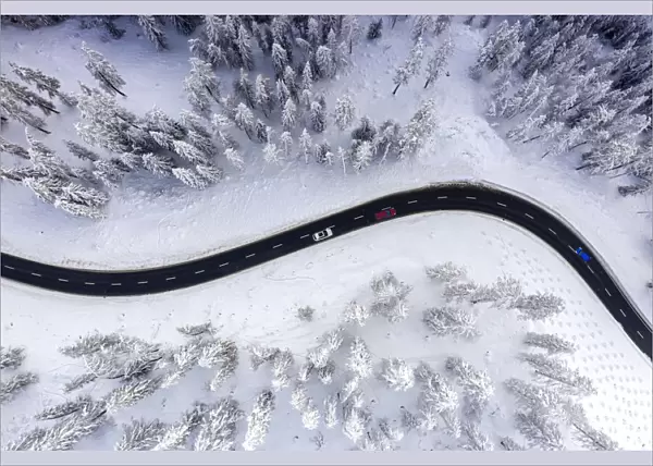 Aerial view of cars traveling on winding mountain road crossing the snow capped woods in