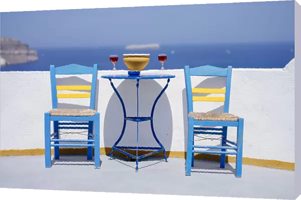Chairs and table with two glasses of red wine against sea, Santorini, Cyclades