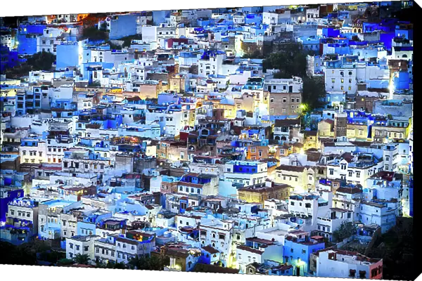 Illuminated crowded blue houses of Chefchaouen viewed from a hill at night, Morocco