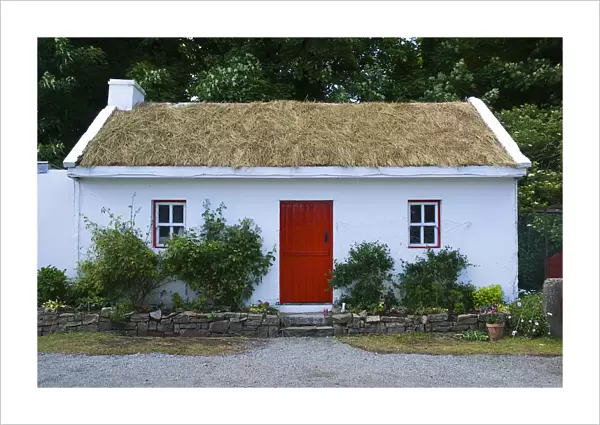 White painted cottage at Sligo Folk Park with red door and turf roof