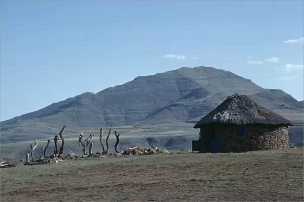 20075183. LESOTHO Architecture Circular straw roofed hut with mountains behind
