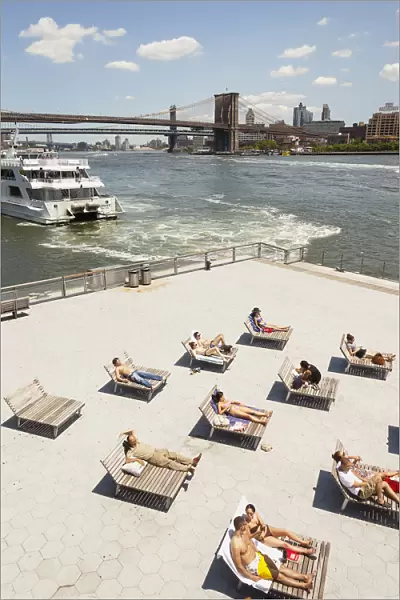 People sunbathing beside East River, Brooklyn Bridge and South Street Seaport, Manhattan