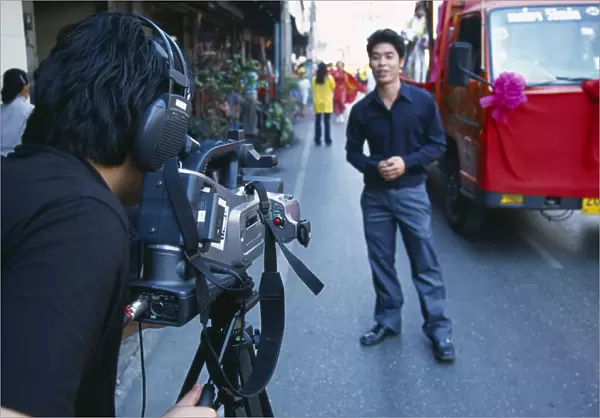 Thailand, North, Chiang Mai, Man with professional video camera aimed at man standing by the road