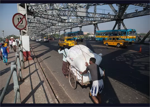 India, West Bengal, Kolkata, Men push a cart loaded with goods across Howrah Bridge