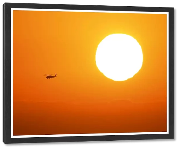 A U. S. military helicopter travels over the pacific ocean past a setting sun near Cardiff