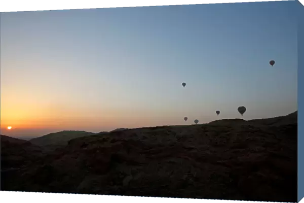 Hot-air balloons carrying tourists fly at sunrise over the city of Luxor