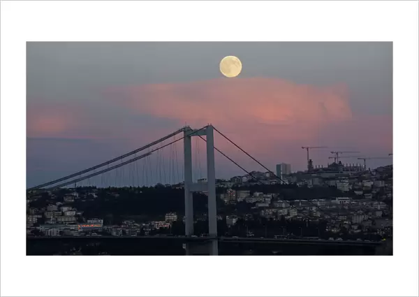 A full moon rises over the Bosphorus bridge in Istanbul