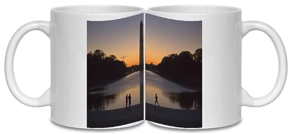 A couple and a jogger pass by the Lincoln Memorial Reflecting Pool before sunrise