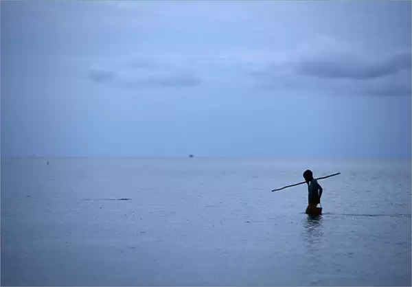 A boy watches for fish as he spear fishes near Larantuka beach