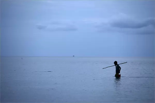A boy watches for fish as he spear fishes near Larantuka beach