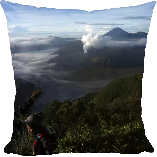 A visitor walks as Indonesias Mount Bromo volcano spew smoke next to Mount Semeru