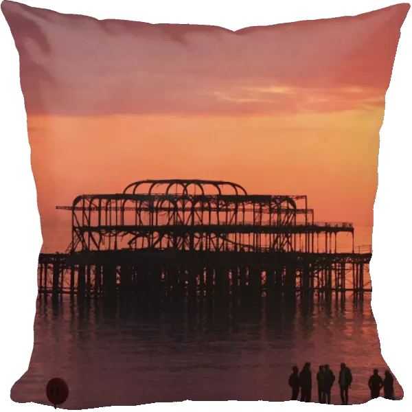 Visitors watch the sun set behind the remains of the West Pier on the seafront at Brighton