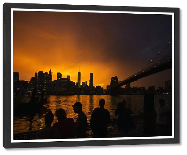 People line a dock in Brooklyn to watch the sun set behind the Manhattan skyline after
