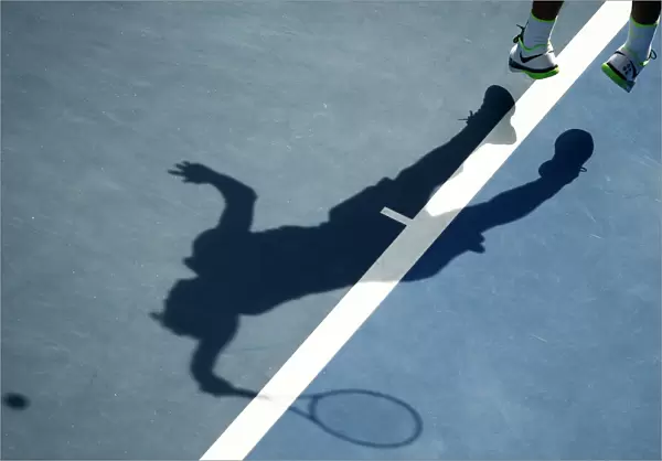 A tennis player casts a shadow as he serves