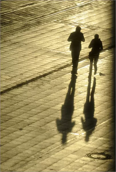 Women cast their shadows in the setting sun as they walk past the headquarters of